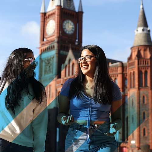 Two students stood in front of brick building with old clock tower