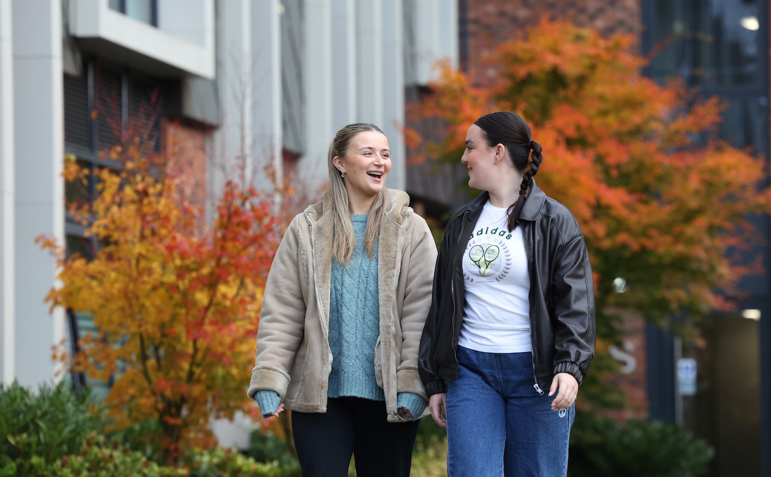 Two students walking outside past two trees with orange leaves